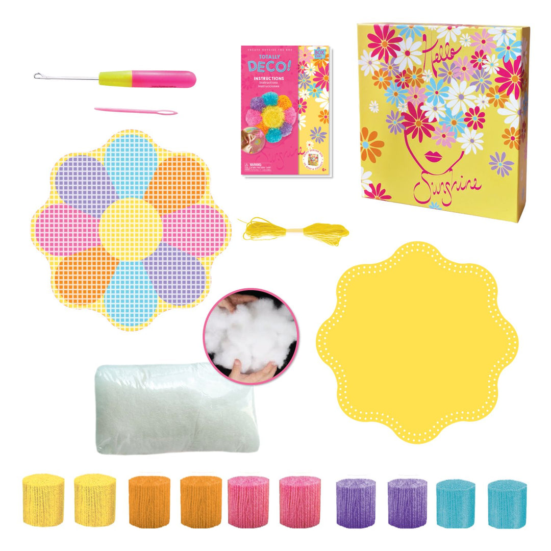 Out of box image of contents included in Totally Deco! Daisy Latch Hook Pillow Set containing 10 rolls of pre-cut colored yarn, 1 latch hook tool, 1 latch hook canvas mat with daisy print, 1 felt mat, 1 crafting needle, sewing thread, cotton stuffing and instructions, all in a keepsake storage box made from recycled cardboard.