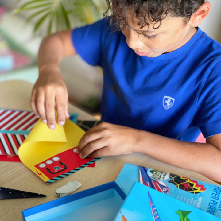 Lifestyle image of a child smiling showing his finished paper airplane.  Edit alt text