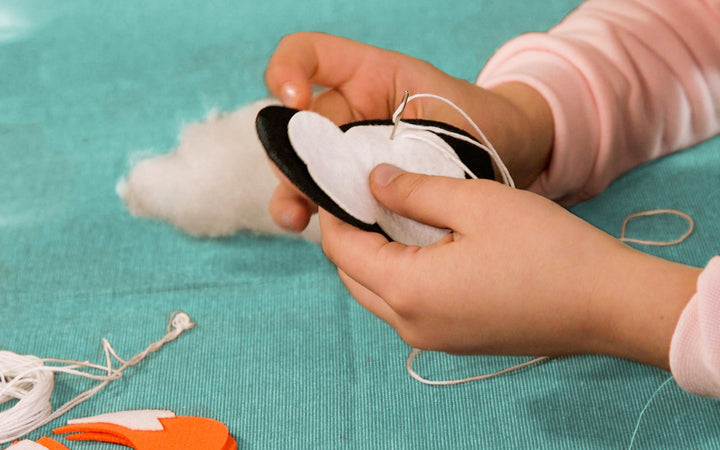Image of a person sewing the penguin ornament together. 