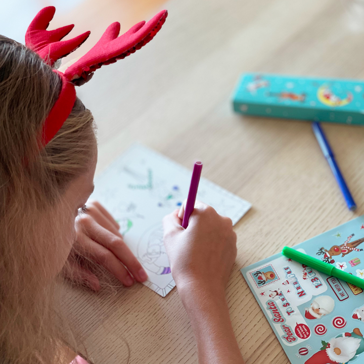 Lifestyle image of a child using the markers to decorate a holiday postcard. 