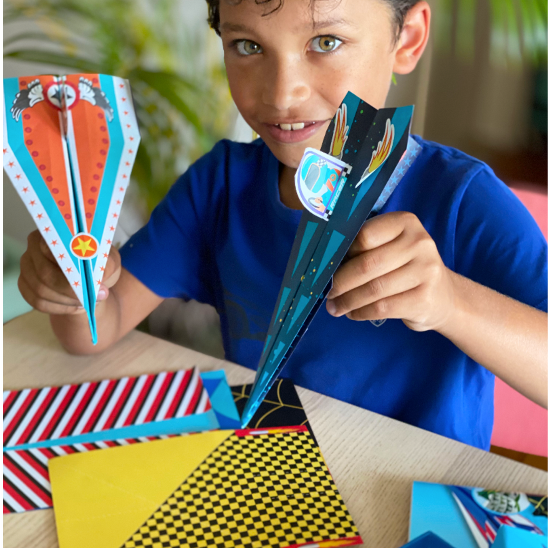 Lifestyle image of a child smiling showing his finished paper airplane.  Edit alt text